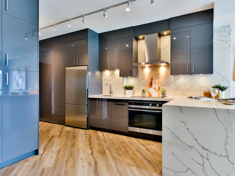 Dark modular kitchen with marble waterfall island, track lights and warm oak flooring