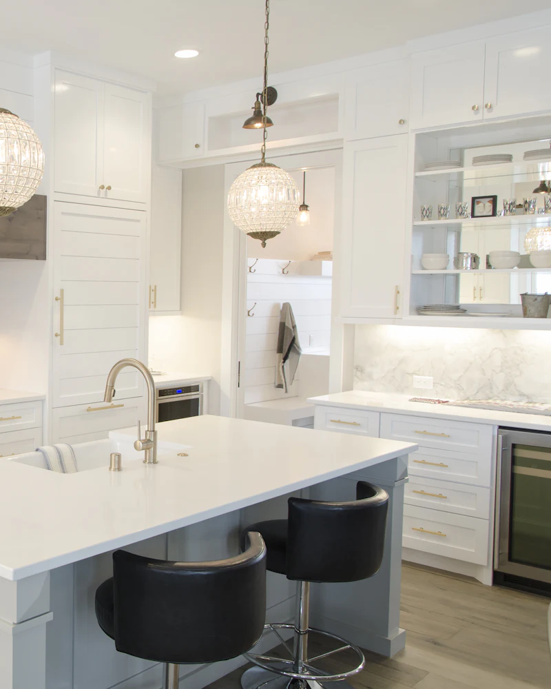 White shaker kitchen with a quartz island, glass pendant lights and black bar stools