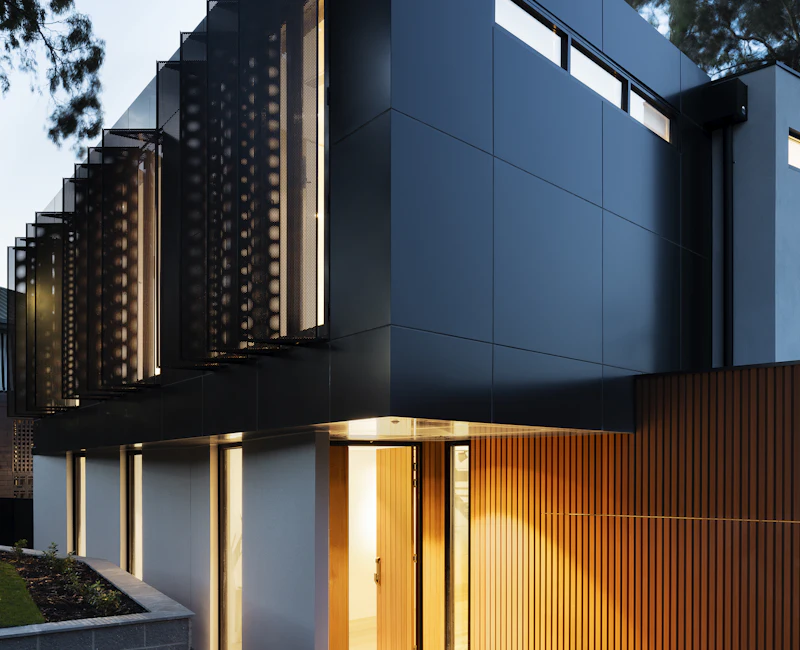Contemporary villa façade with dark cladding, vertical timber screens and warm evening lighting